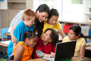 Teacher with five students at desk using laptop